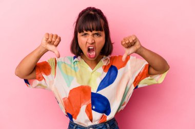 Pembe arka planda izole edilmiş genç melez kadın baş parmağını aşağı gösteriyor ve hoşlanmadığını ifade ediyor..