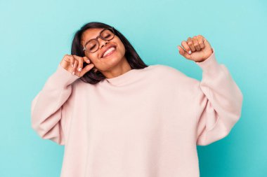 Mavi arka planda izole edilmiş genç Latin kadın özel bir günü kutluyor, atlıyor ve enerjiyle kollarını kaldırıyor..