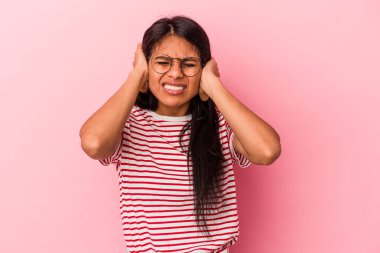 Pembe arka planda izole edilmiş genç Latin kadın kulaklarını elleriyle kapatıyor..