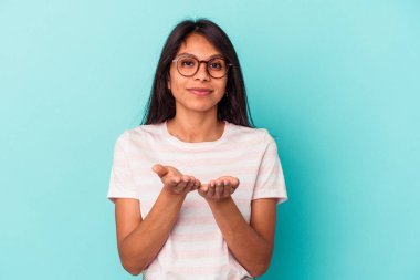 Mavi arka planda izole edilmiş genç Latin bir kadın elinde avuç içi bir şeyle kameraya sunuyor..