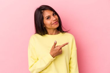 Pembe arka planda izole edilmiş genç Latin kadın gülümsüyor ve boş alanda bir şeyler gösteriyor..