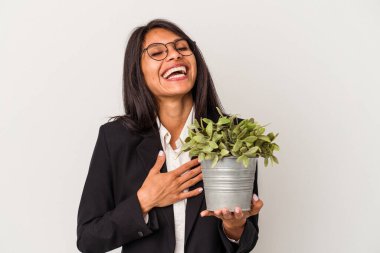 Beyaz arka planda saklanmış bitkileri tutan genç Latin kadın kahkahalarla gülüyor..