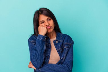 Mavi arka planda izole edilmiş, üzgün ve dalgın hisseden genç Latin kadın fotokopi odasına bakıyor..