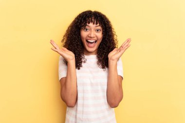 Sarı arka planda izole edilmiş genç melez bir kadın zaferi ya da başarıyı kutluyor, şaşırıyor ve şok oluyor..