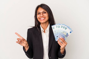 Beyaz arka planda izole edilmiş banknotlar tutan genç Latin kadın gülümsüyor ve boş alanda bir şeyler gösteriyor..