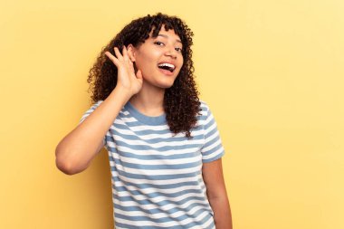 Sarı arka planda izole edilmiş genç melez kadın bir dedikoduyu dinlemeye çalışıyor..