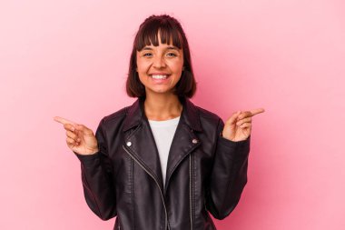 Pembe arka planda izole edilmiş genç bir ırk kadını farklı kopya alanlarını gösteriyor, birini seçiyor, parmaklarıyla gösteriyor..