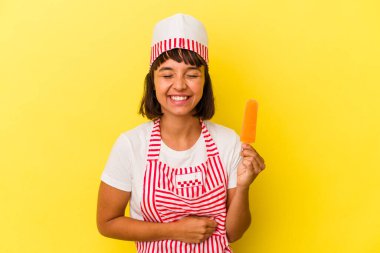 Genç melez dondurma üreticisi kadın dondurma tutuyor sarı arka planda izole edilmiş gülüyor ve eğleniyor..