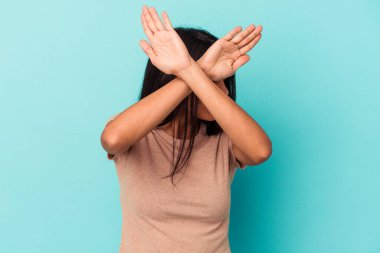 Mavi arka planda izole edilmiş genç Latin kadın iki kolu çapraz tutuyor, inkar kavramı.