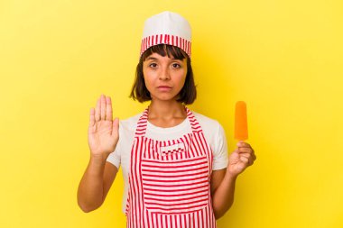 Genç melez dondurma üreticisi elinde dondurma tutan kadın sarı arka planda izole edilmiş, uzanmış elinde dur işareti olan, seni engelleyen.