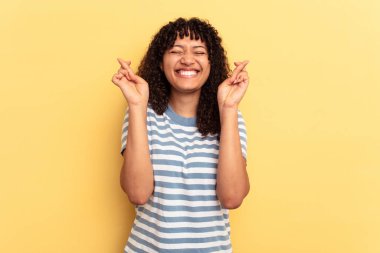 Sarı arka planda izole edilmiş genç melez kadın şans getirsin diye dua ediyor.