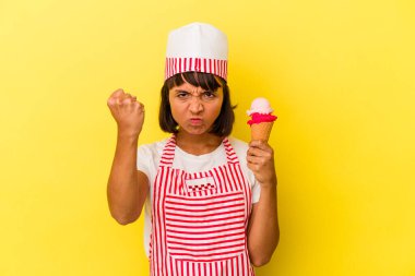 Küçük melez dondurma üreticisi kadın elinde dondurma tutuyor sarı arka planda izole edilmiş kameraya yumruğunu gösteriyor, agresif yüz ifadesi var..