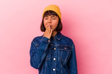 Pembe arka planda soyutlanmış genç melez bir kadın esniyor. Ağzıyla ağzını kapatan yorgun bir hareket sergiliyor..