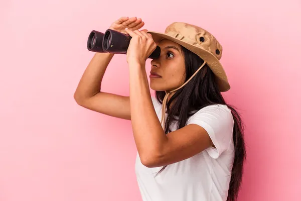 年轻的拉丁女子手持双筒望远镜 从粉色背景分离出来 — 图库照片