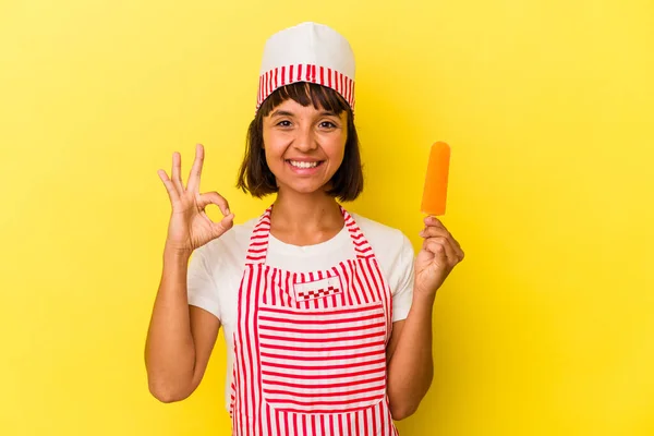 年轻的混合种族冰淇淋制造商女人拿着一个黄色背景的冰淇淋 快乐而自信地做出了一个好的手势 — 图库照片