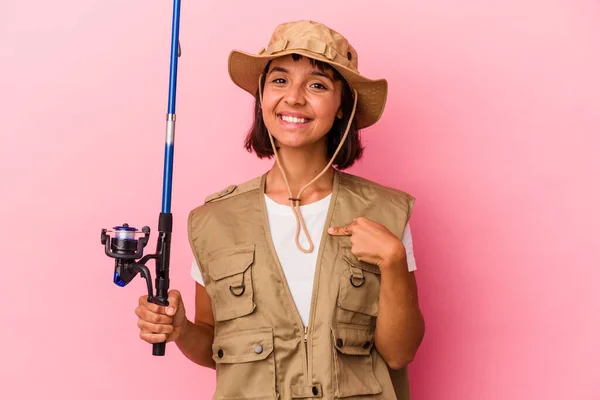 年轻的混血女渔夫拿着一根杆子 与粉色背景的人隔离在一起 手拿着一件衬衫的复制品 自豪而自信 — 图库照片