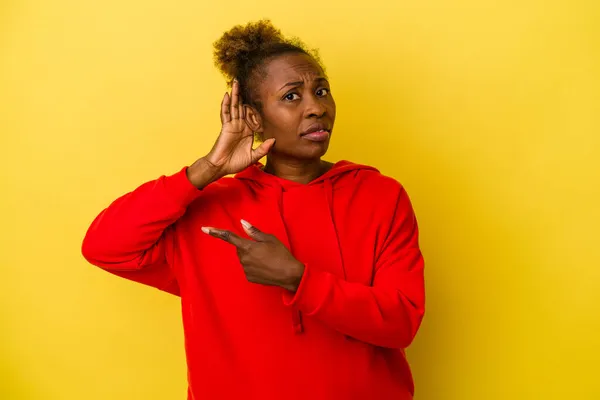 Young african american woman isolated on yellow background trying to listening a gossip.