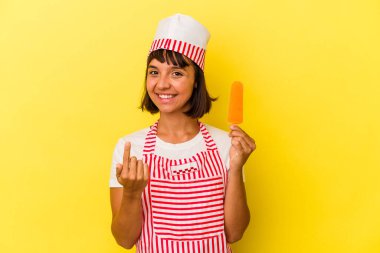 Genç melez dondurma üreticisi kadın sarı arka planda izole edilmiş dondurma tutuyor. Sanki seni davet ediyormuş gibi..