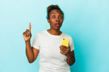 Genç Afrikalı Amerikalı bir kadın cep telefonunu mavi arka planda izole etmiş. Bir fikri var, ilham verici bir kavram..