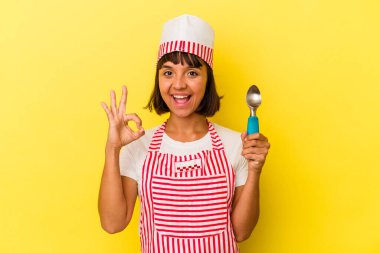 Genç melez dondurma üreticisi kadın sarı arka planda izole edilmiş bir dondurma tutuyor. Genç melez dondurma üreticisi kadın sarı arka planda izole edilmiş bir dondurma kepçesi tutuyor. Neşeli ve kendinden emin..