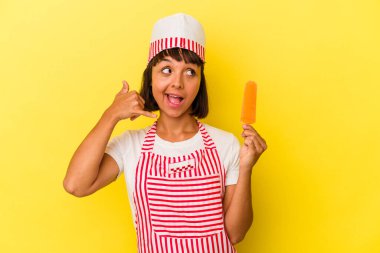 Küçük melez dondurma üreticisi kadın, sarı arka planda izole edilmiş dondurma tutuyor. Cep telefonu hareketini parmaklarıyla gösteriyor..