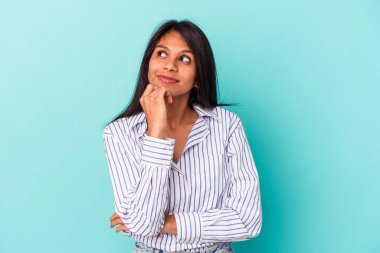 Mavi arka planda izole edilmiş genç Latin bir kadın rahatlamış bir şeyin fotokopi odasına baktığını düşünüyor..