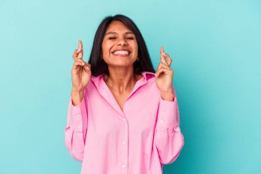 Mavi arka planda izole edilmiş genç Latin kadın şans getirsin diye dua ediyor.