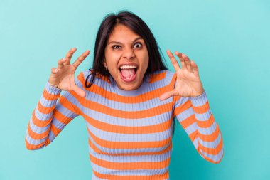 Mavi arka planda izole edilmiş genç Latin kadın pençelerini bir kediyi taklit ederken gösteriyor, agresif bir hareket..