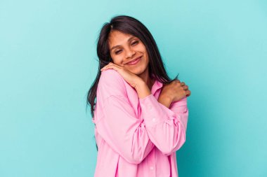 Mavi arka planda yalnız kalmış genç Latin bir kadın. Kucaklaşma, kaygısız gülümseme ve mutluluk..