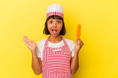 Genç melez dondurma üreticisi elinde dondurma tutan kadın sarı arka planda izole edilmiş şaşırmış ve şok olmuş..