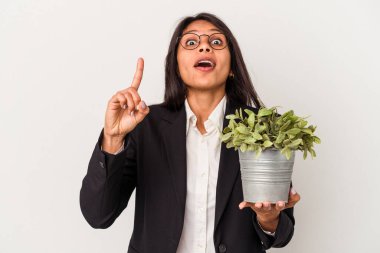 Beyaz arka planda bitkileri tutan genç Latin kadın bir numarayı parmaklarıyla gösteriyor..