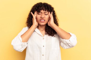 Sarı arka planda izole edilmiş genç melez kadın şakaklara dokunuyor ve başı ağrıyor..