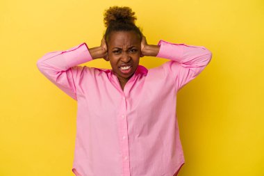 Genç Afro-Amerikalı kadın sarı arka planda izole edilmiş kulakları kulaklarıyla kapatıyor çok fazla ses duymamaya çalışıyor..