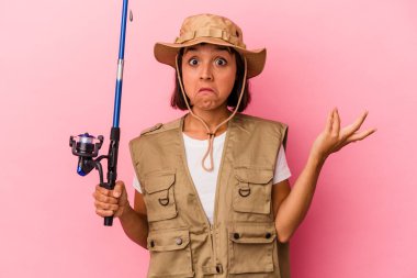 Genç melez balıkçı pembe arka planda izole edilmiş bir çubuk tutuyor omuzlarını silkiyor ve gözleri açık..