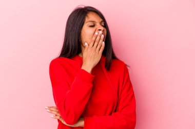 Pembe arka planda izole edilmiş genç Latin kadın esniyor. Ağzı eliyle kapatan yorgun bir jest gösteriyor..