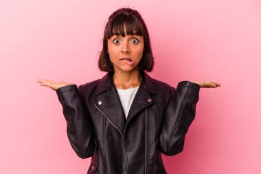 Pembe arka planda soyutlanmış genç melez bir kadın. Kopya alanını tutmak için kafası karışık ve omuz silkiyor..