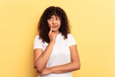 Sarı arka planda izole edilmiş genç melez kadın şüpheli ve şüpheci bir ifadeyle yana bakıyor..