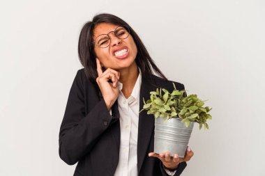Beyaz arka planda bitkileri tutan genç Latin kadın kulaklarını elleriyle kapatıyor..
