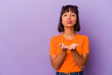 Mor arka planda izole edilmiş genç melez bir kadın dudakları katlıyor ve hava öpücüğü göndermek için avuç içleri tutuyor..