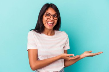 Mavi arka planda izole edilmiş genç Latin bir kadın avucunun içinde bir kopya alanı tutuyor..