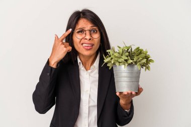 Beyaz arka planda bitkileri tutan genç Latin kadın işaret parmağıyla hayal kırıklığı gösteriyor..
