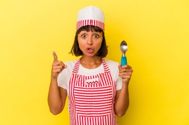 Genç melez dondurma üreticisi kadın elinde sarı arka planda izole edilmiş dondurma tutuyor. Genç melez dondurma üreticisi kadın sarı arka planda izole edilmiş bir dondurma kepçesi tutuyor. Bir fikri var, ilham verici bir kavram..