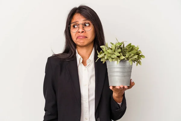 Young business latin woman holding plants isolated on white background confused, feels doubtful and unsure.