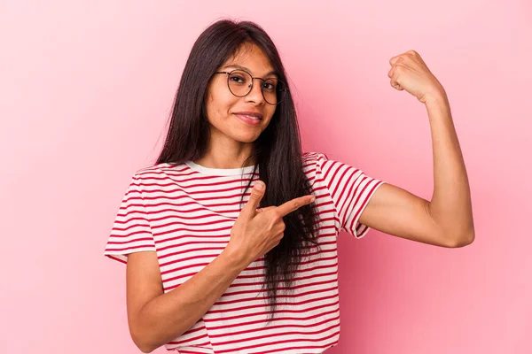 Pembe arka planda izole edilmiş genç Latin kadın güçlü bir hareket gösteriyor, kollarıyla, kadınsı gücün sembolü.