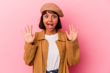 Pembe arka planda soyutlanmış genç melez bir kadın hoş bir sürprizle karşılaşıyor, heyecanlı ve el kaldırıyor..