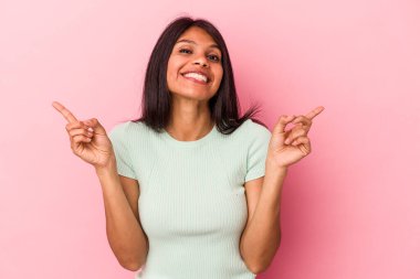 Pembe arka planda izole edilmiş genç Latin bir kadın farklı kopya alanlarını gösteriyor, birini seçiyor, parmaklarıyla gösteriyor.