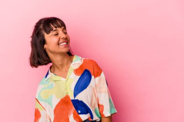 Genç melez bir kadın pembe arka planda izole edilmiş rahat ve mutlu bir şekilde gülüyor, boynunda dişlerini gösteriyor..