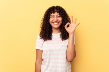 Sarı arka planda izole edilmiş genç melez bir kadın neşeli ve kendinden emin, iyi bir hareket gösteriyor..