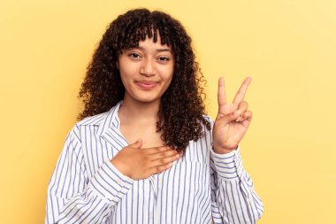 Genç melez kadın sarı arka planda izole edilmiş yemin ediyor, elini göğsüne koyuyor..