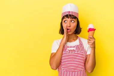 Sarı arka planda izole edilmiş dondurma tutan genç melez dondurma üreticisi kadın gizli bir sıcak fren haberi veriyor ve yan bakıyor.